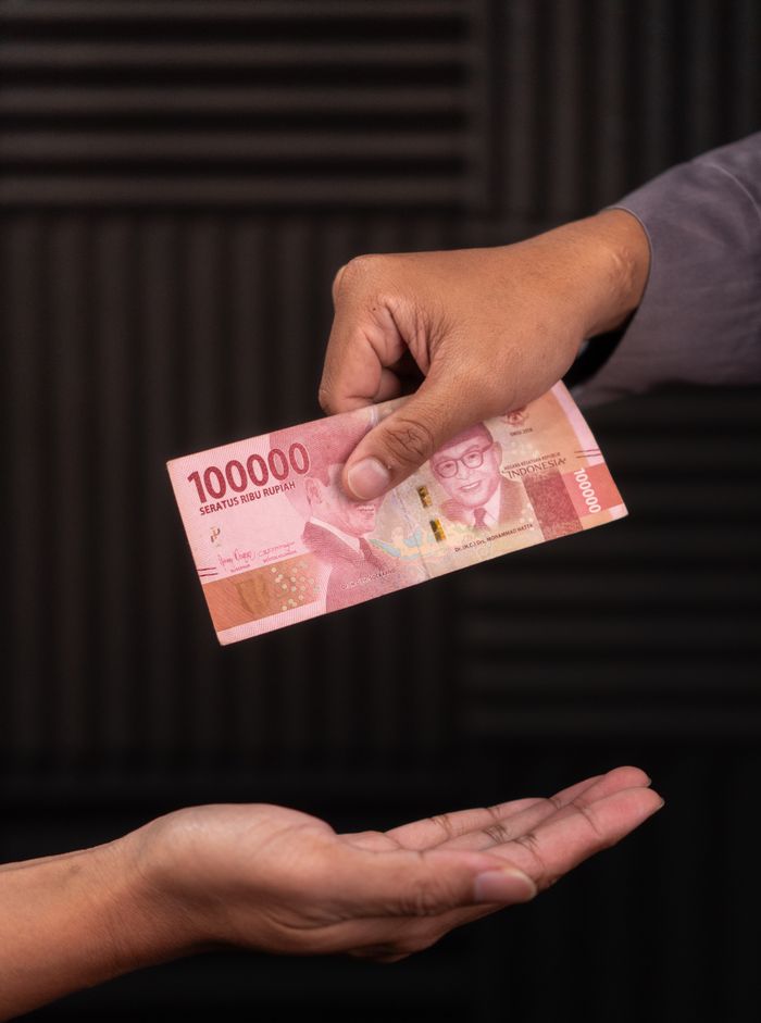 Close-up of hands exchanging 100,000 Indonesian Rupiah note, symbolizing charity and giving.